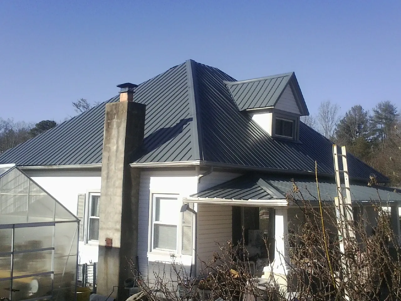 Dark blue standing seam metal roof on a white farmhouse with dormer — Slate & Tile Roof Repair by Roofing Brothers in Farmingville