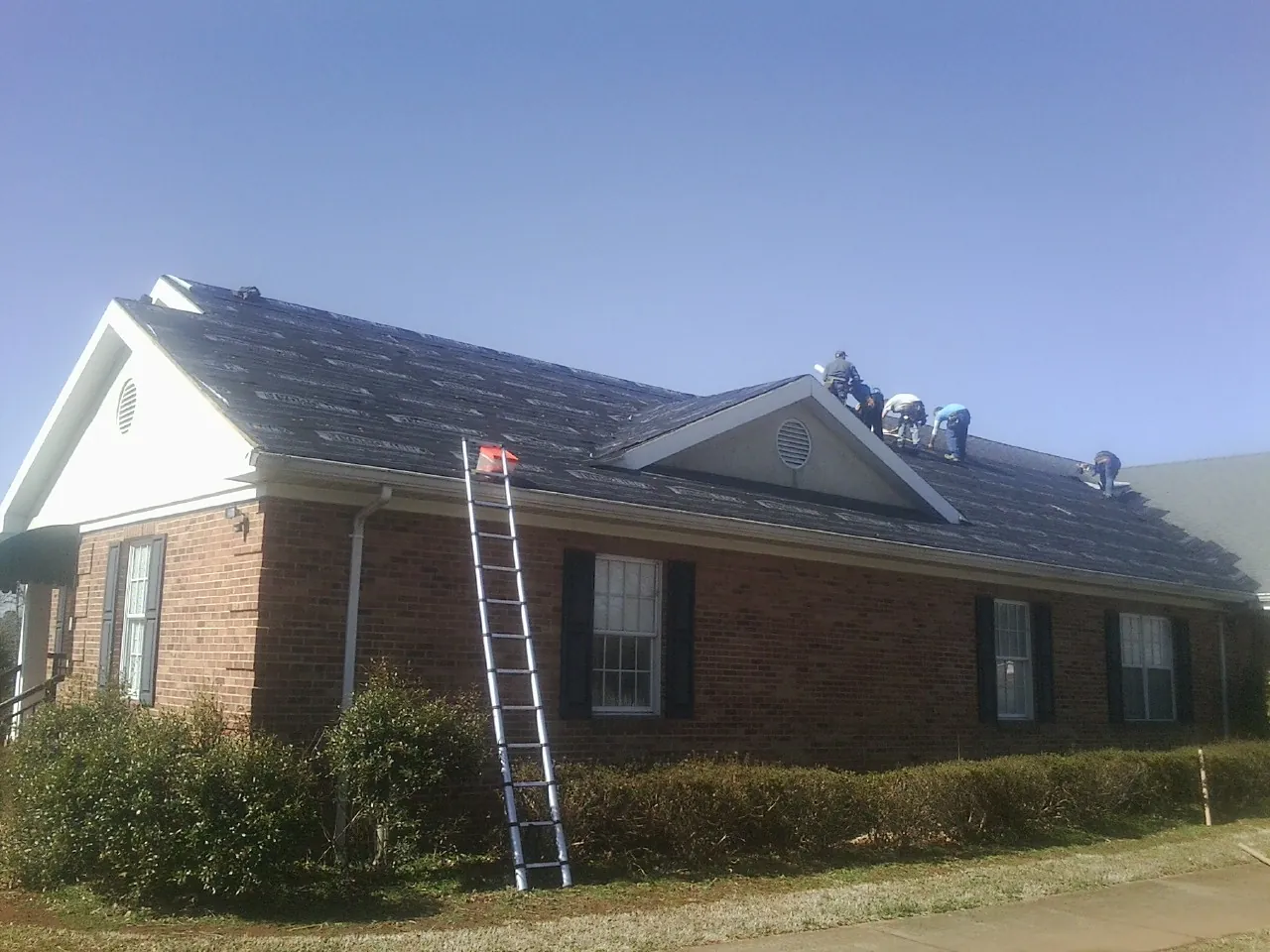 Crew tearing shingles off a brick ranch roof with a ladder set — Emergency Roof Repair work by our crew in Farmingville