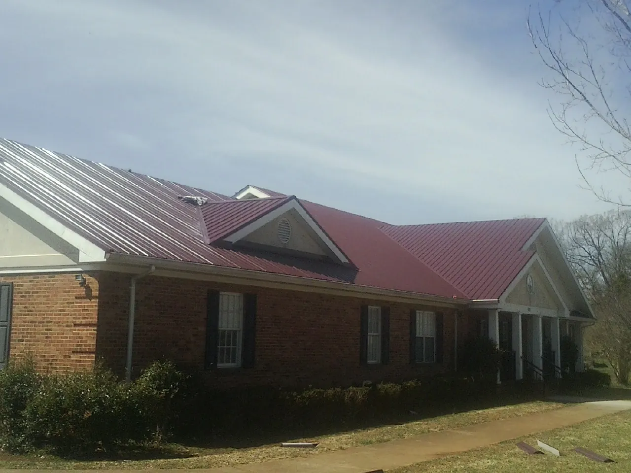 Red metal roof with gabled entries on a long brick building, from a Hail Damage Roof Repair job in Farmingville