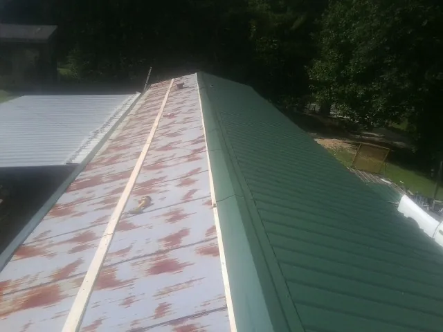 Old rusted panels beside newly installed green metal roofing — Wind Damage Roof Repair by Roofing Brothers in Farmingville