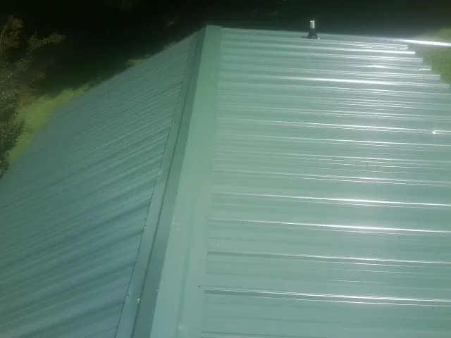 New green metal panels meeting at the ridge of a roof — Flat Roof Repair work by our crew in Farmingville