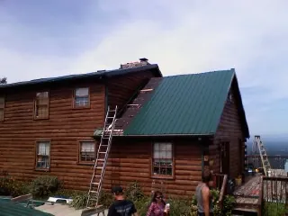 Green metal roof going on a two story log home with ladders set in Farmingville