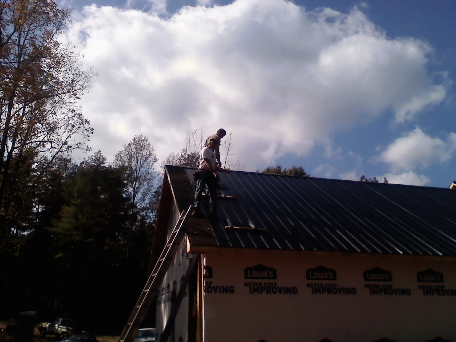 Roofer fastening dark metal panels high against a cloudy sky, from a Roof Inspection job in Farmingville
