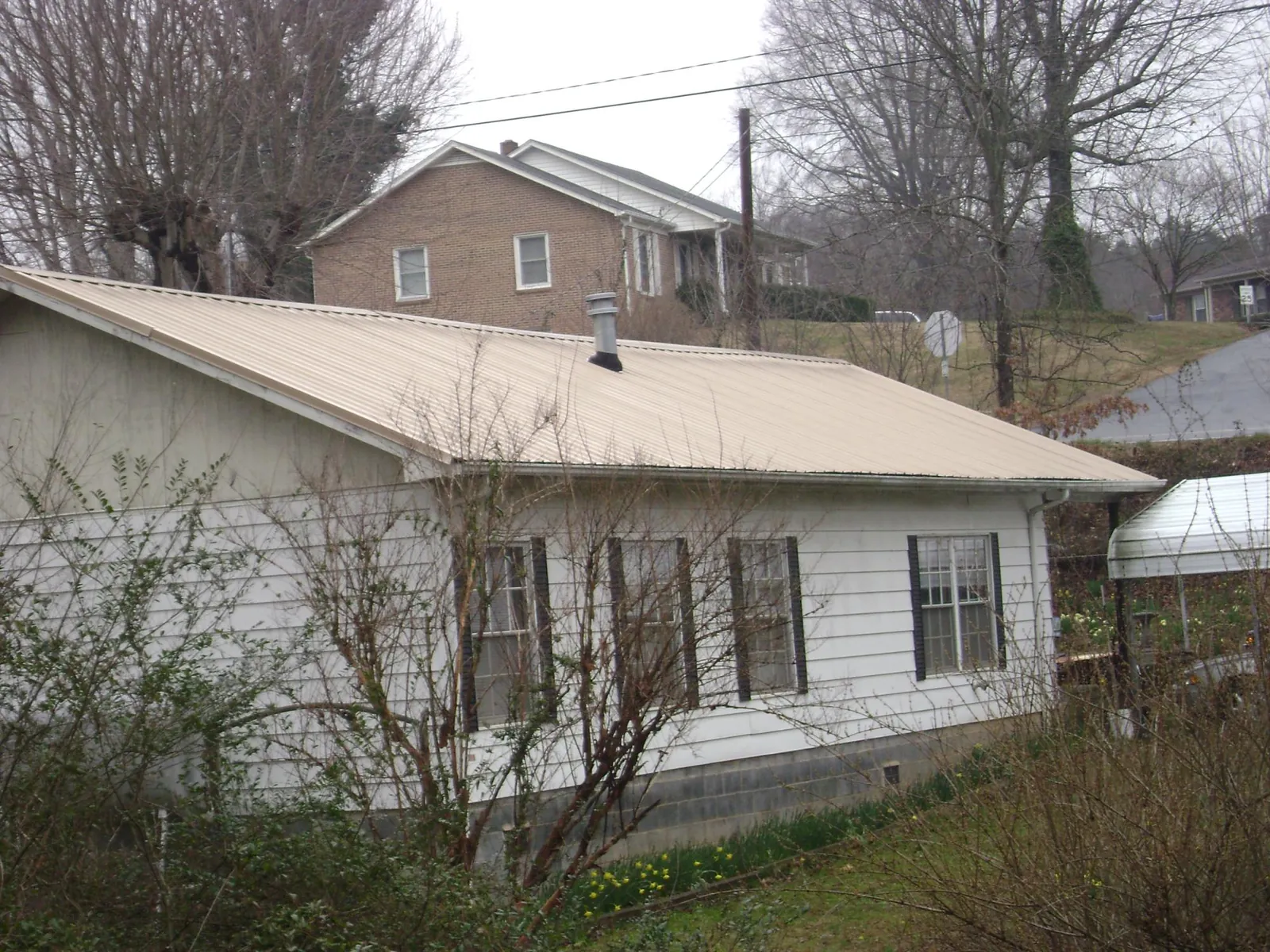 Tan metal roof on a white sided house set into a hillside — Commercial Roofing by Roofing Brothers in Farmingville