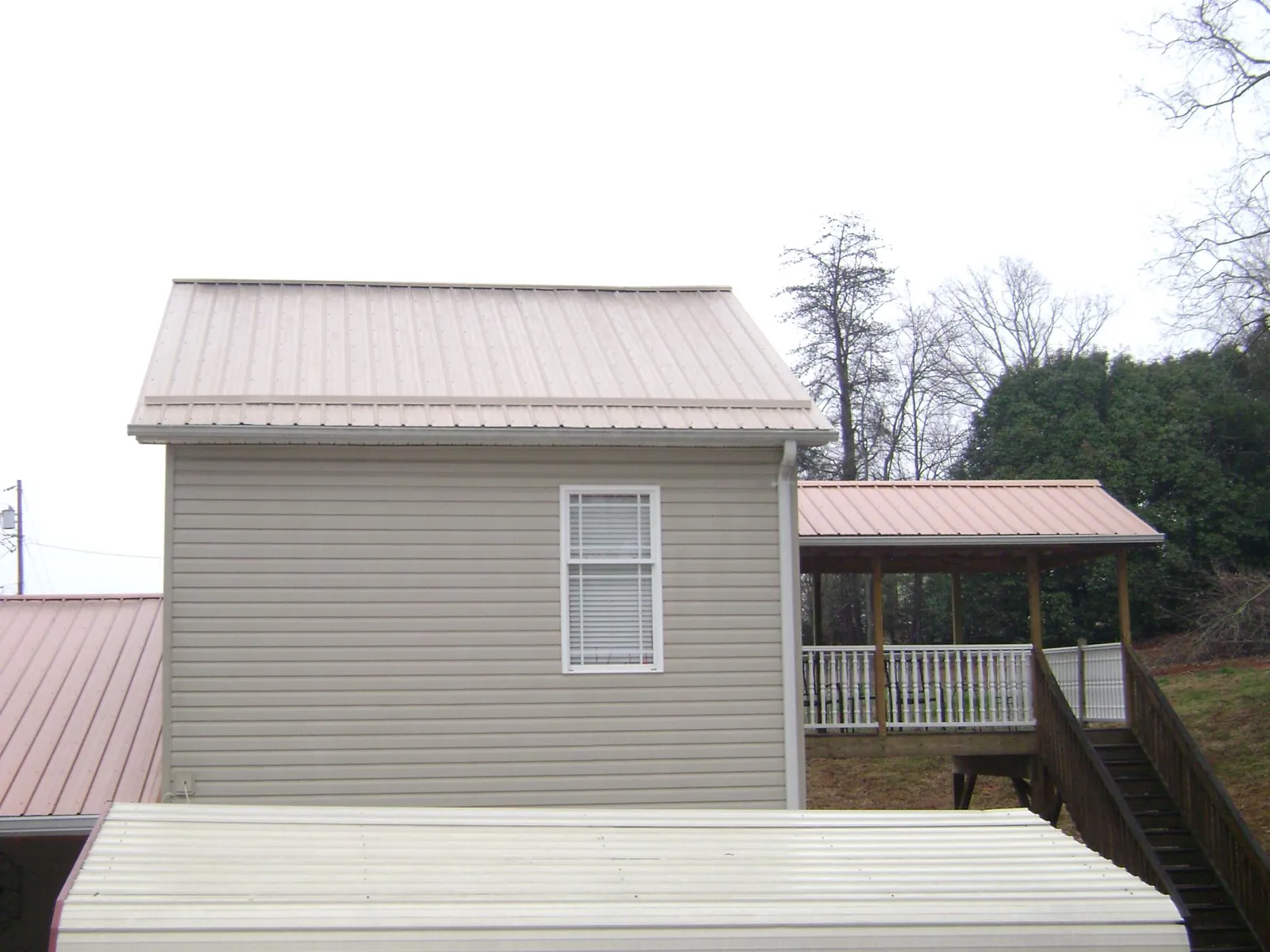 Tan metal roofs on a two story addition and attached porch, from a Roof Replacement job in Farmingville